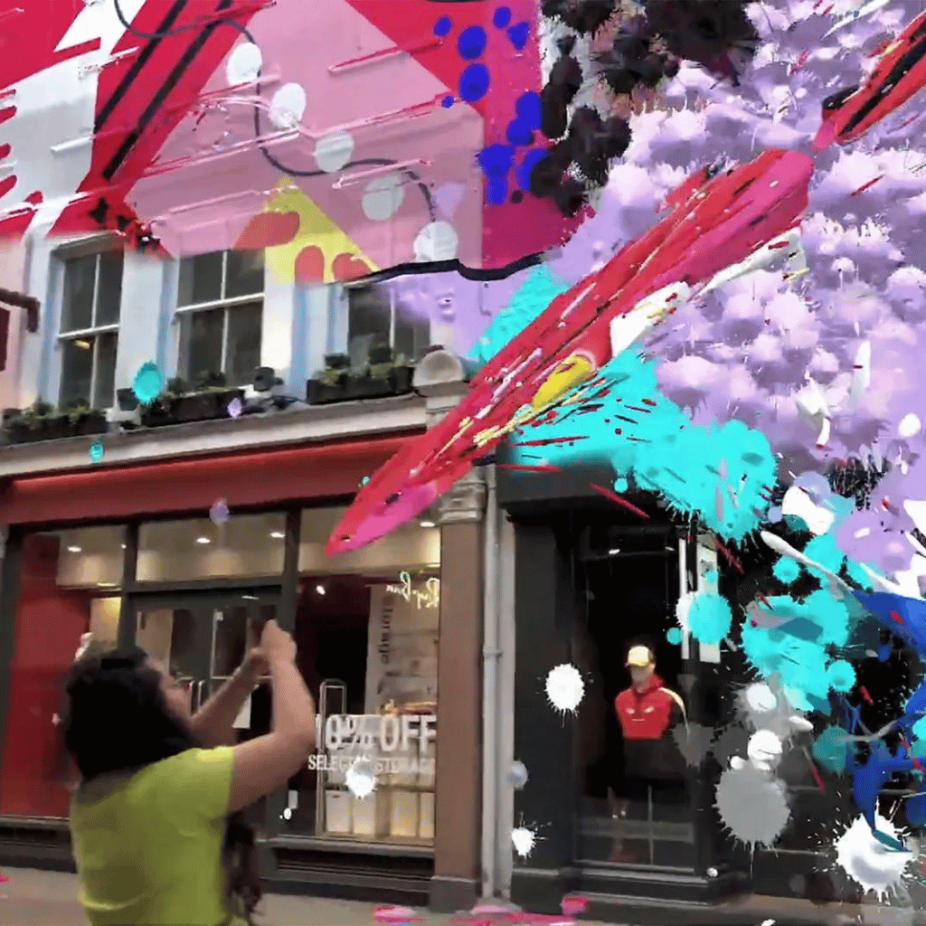 A person experiences an augmented reality (AR) explosion of vibrant paint splashes in the air outside a retail store, showcasing an interactive marketing display.