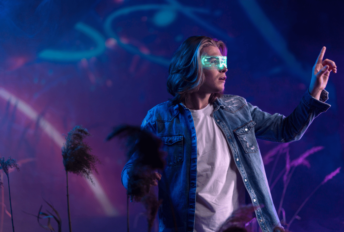 A person with light-colored hair wears futuristic glasses displaying graphics, standing in a neon-lit space with an extended hand as if interacting with a virtual interface.