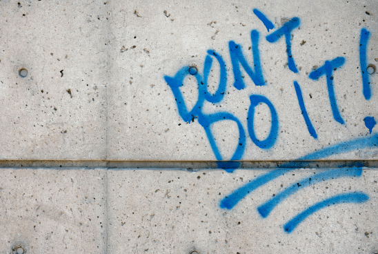 Graffiti on a concrete wall with the phrase "DON'T DO IT!" sprayed in blue paint.