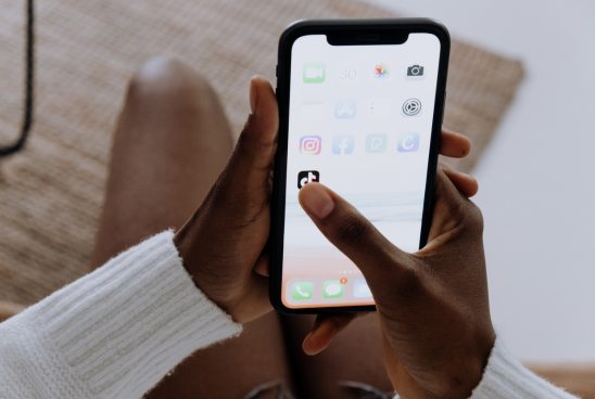 Hands holding a smartphone displaying a variety of popular apps on the home screen.