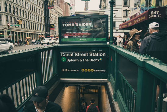 Busy urban scene at Canal Street Station with a prominently displayed "Tomb Raider" advertisement overhead.