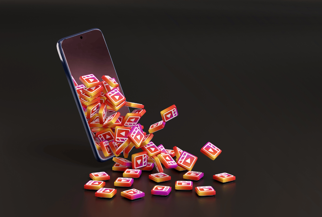 A smartphone on its side with a stream of colorful Instagram Reel icons spilling out onto a dark surface.