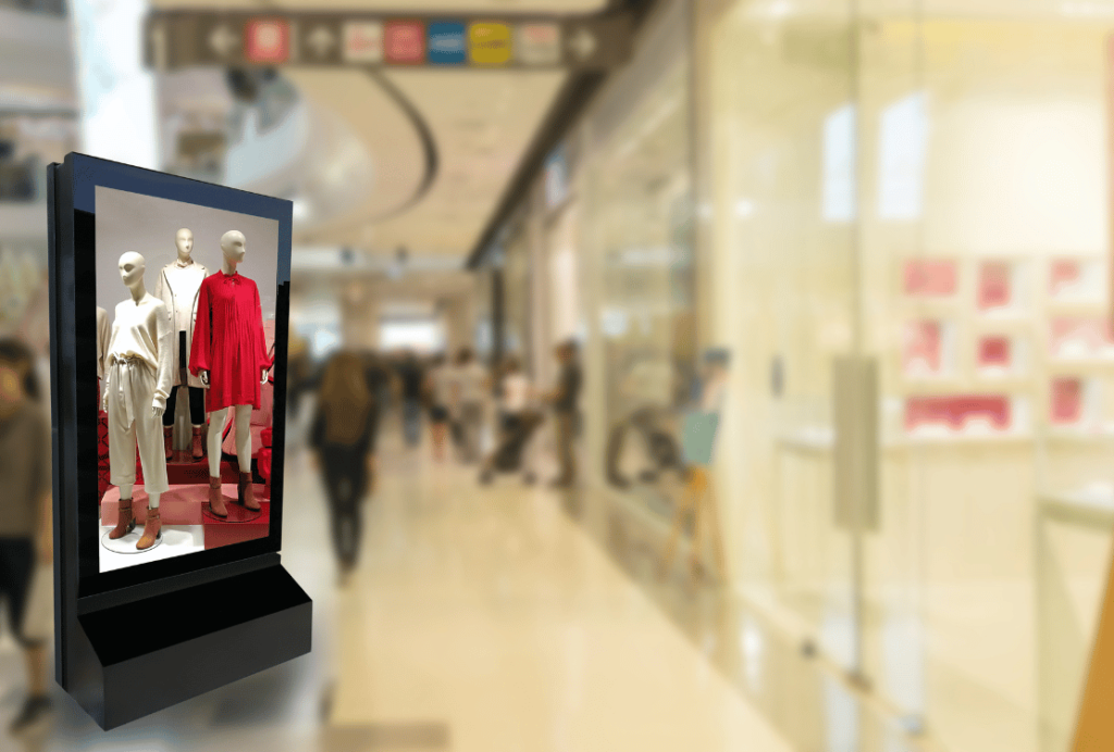 A focused display of mannequins in a shopping mall, with one dressed in a striking red outfit, surrounded by the blurred activity of shoppers.