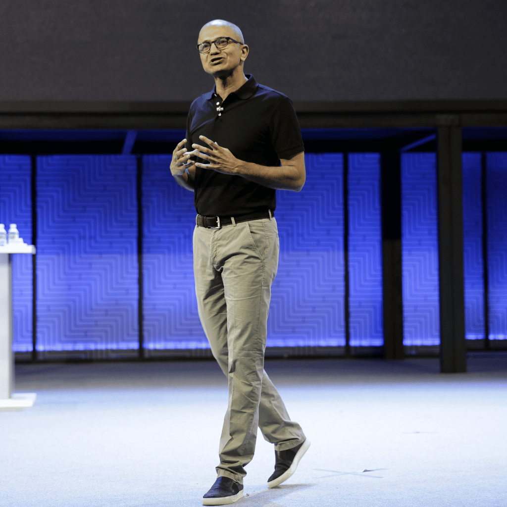 Satya Nadella, CEO of Microsoft, stands confidently on stage, presenting at a tech conference.