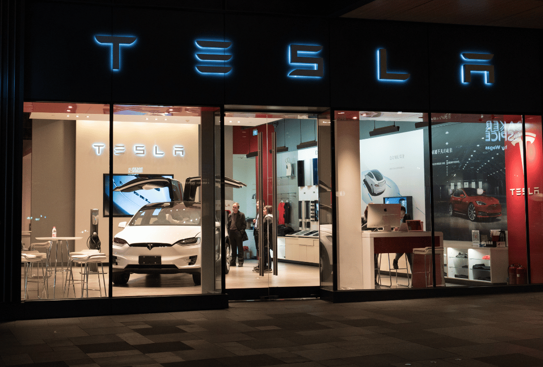 A Tesla showroom glows under neon signage, displaying sleek electric vehicles and modern interior design, inviting onlookers into the world of innovative automotive technology.