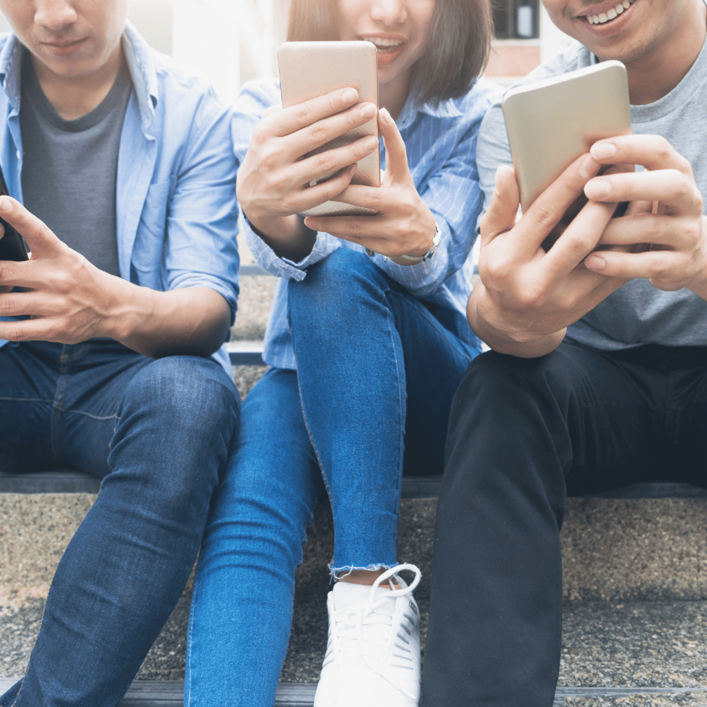 Three friends sitting on steps, each engrossed in their own smartphone, representing the modern way of connecting with companies digitally.