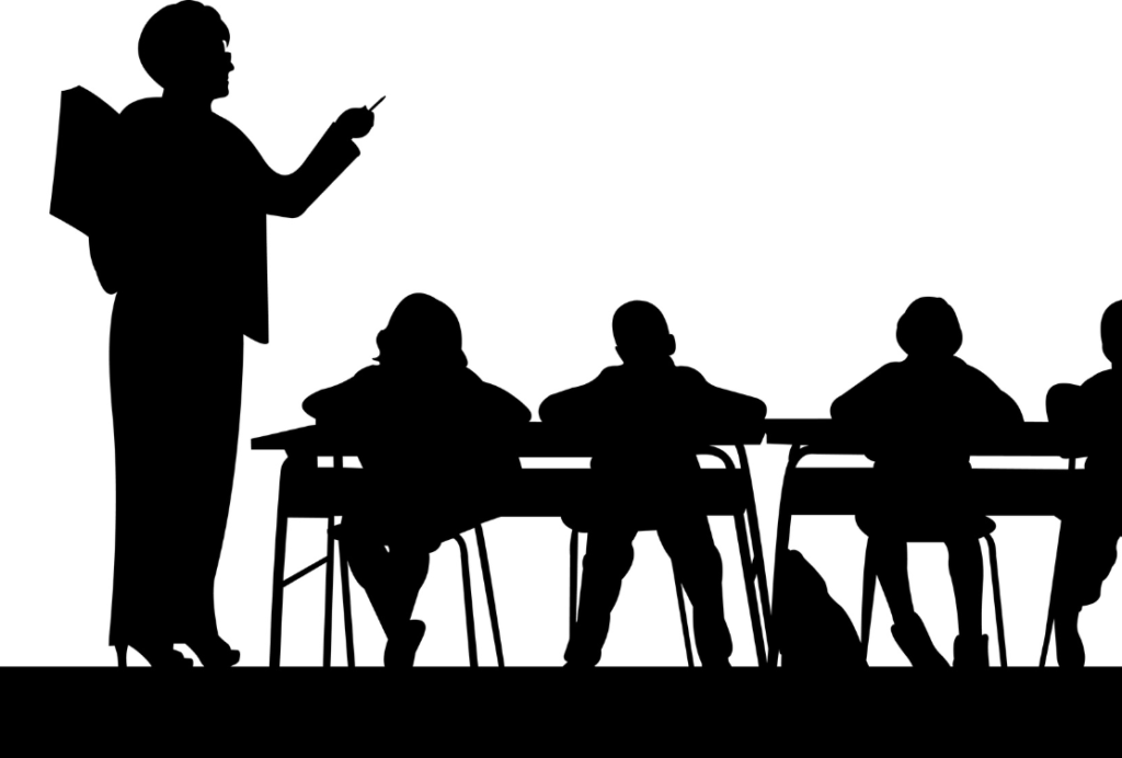 Silhouette of a person standing and presenting to a group seated at a table.