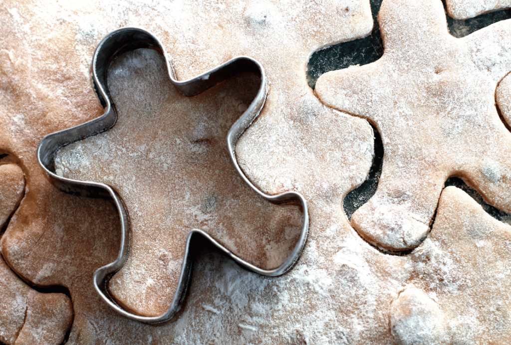 Gingerbread cookie dough with a cookie cutter creating a human shape, surrounded by excess dough.